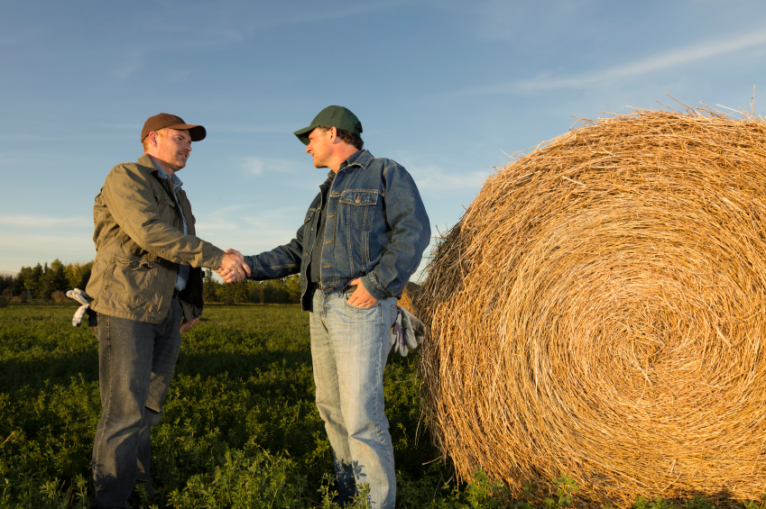Farmers shaking hands next to hay roll
